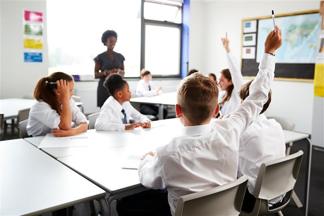 classroom with children in uniforms and raising hands to answer questions