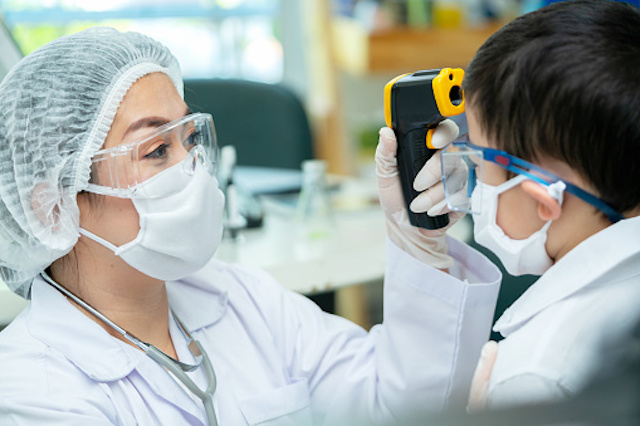 Nurse taking the temperature of a student. Both are wearing face masks. 