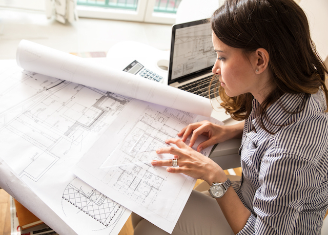 A woman architect looking at blueprints with her laptop open. 