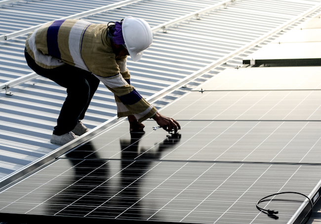 Worker on roof adjusting solar panels. 