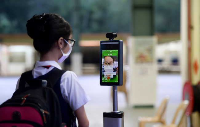 Student wearing a face mask stands in front of thermal imaging device. 