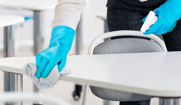 Someone with blue rubber gloves wiping down a desk. 